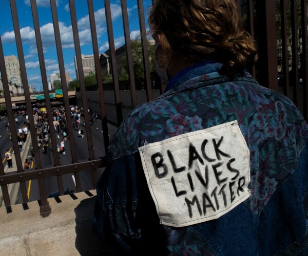 man wearing a blue and purple patterned shirt with a black lives matter patch sewed on