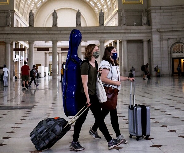 people walk through train station wearing masks