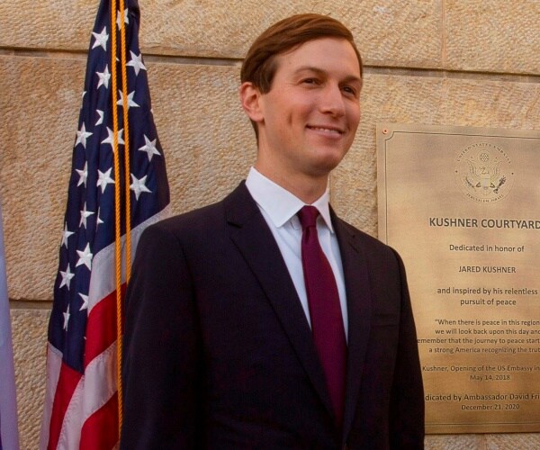 jared kushner stands in front of the u.s. flag next to a plaque in his name.