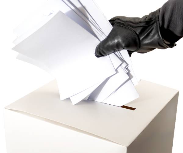 a gloved hand stuffing a ballot box