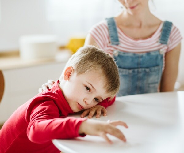 boy sitting with his Mom at a table but not paying attention to her