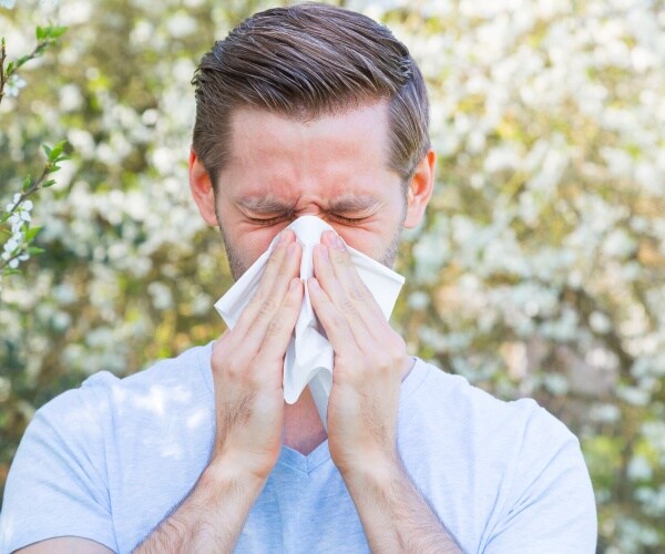 man sneezing while standing near spring flowers