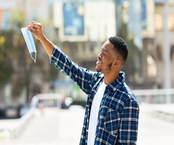 A man outside taking off his mask and smiling