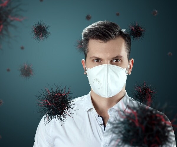 man with surgical mask on and coronavirus particles in air around him