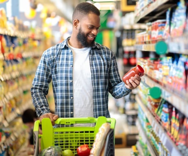 man in grocery store looking at label on tomato sauce