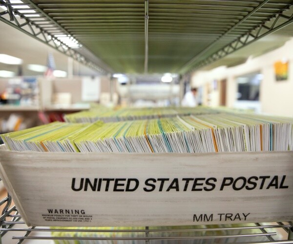 usps bin with a stack of mail-in ballots sitting on a shelf