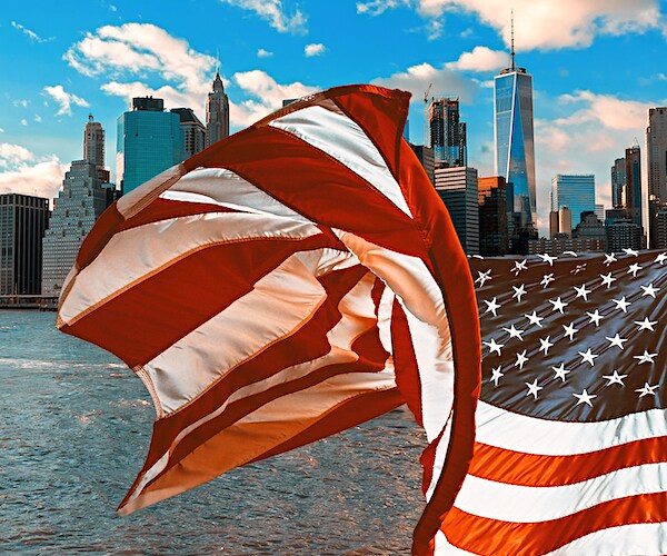 an american flag waves in front of a shot of the new york city skyline