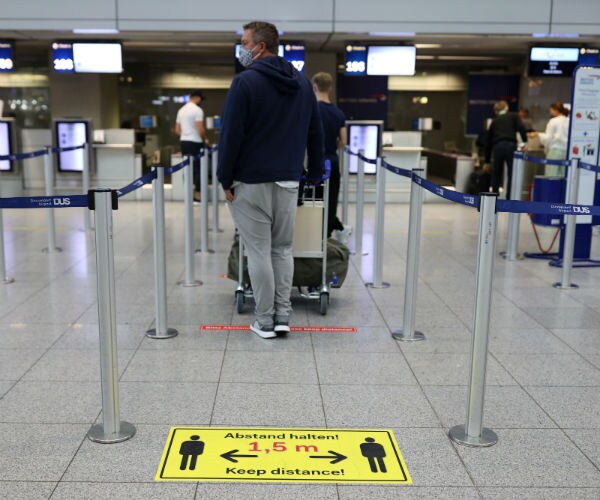 passsengers are shown wearing masks in airport check-in line 