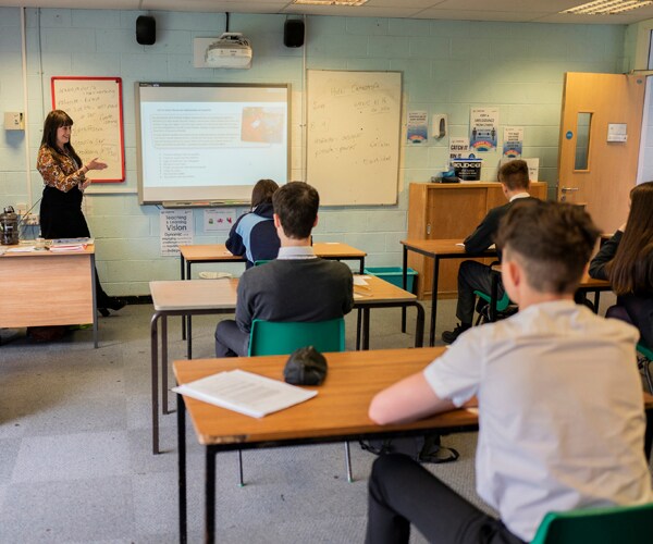 students listen to and watch a teacher in a classroom