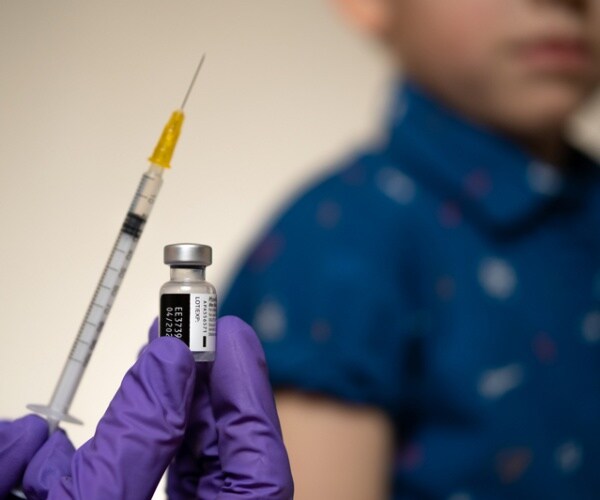 young child in background, Pfizer COVID vaccine vial and syringe