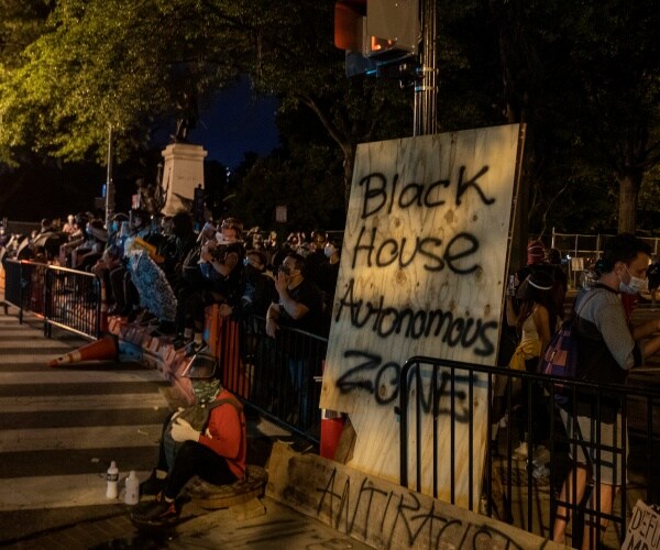 people gather near the jackson statue with "BHAZ" spraypainted on a wooden board