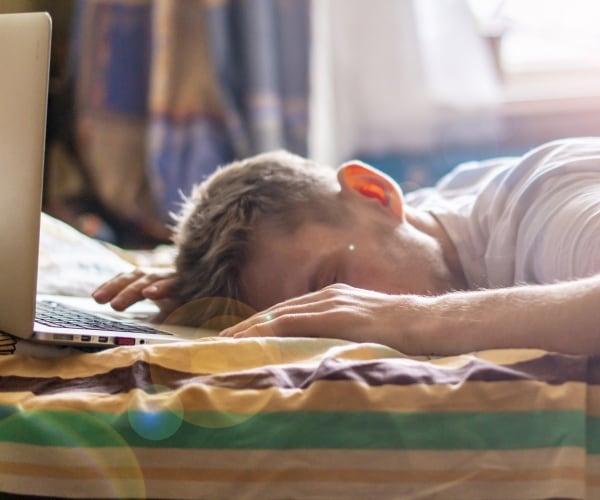 man asleep on laptop in bed in early morning