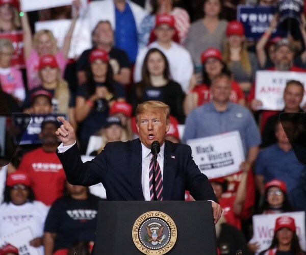 trump speaks in a suit and pink and black striped tie at a campaign rally