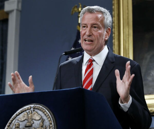 bill de blasio is seen speaking in a dark suit, dress shirt and red and white striped tie