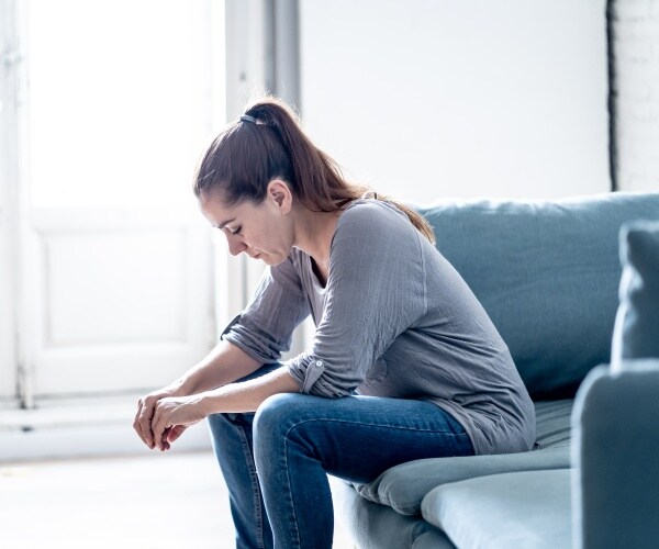 young woman sitting on couch with head down, looking depressed