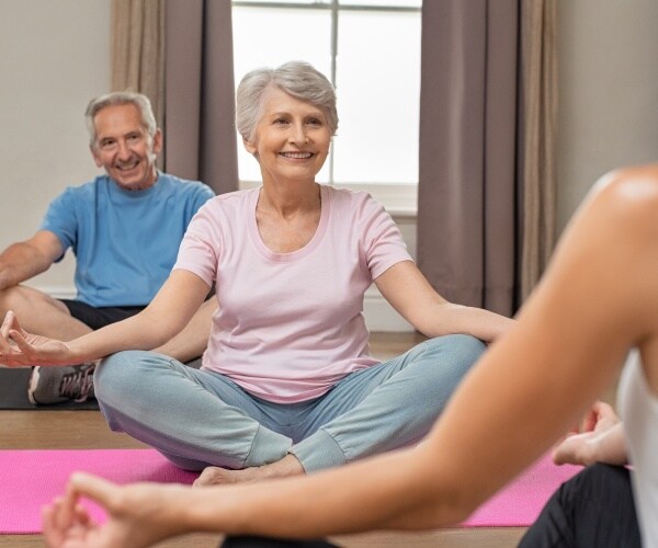 a senior man and woman doing easy yoga/stretching with an instructor