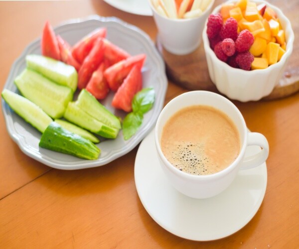 table with a plate of veggies, bowl of fruit and a mug of coffee