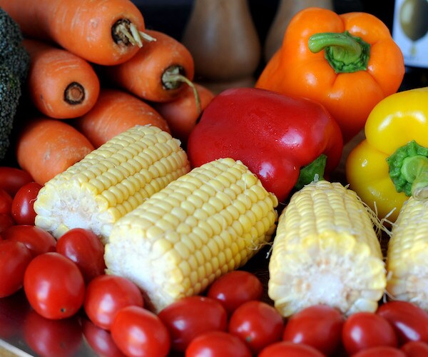 corn, peppers, carrots, and tomatoes are bunched on a table at a farmer's market