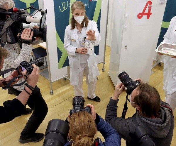 journalists take pictures of a doctor holding up the covid vax