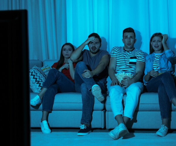 four young adults watching television with horrified looks on their faces