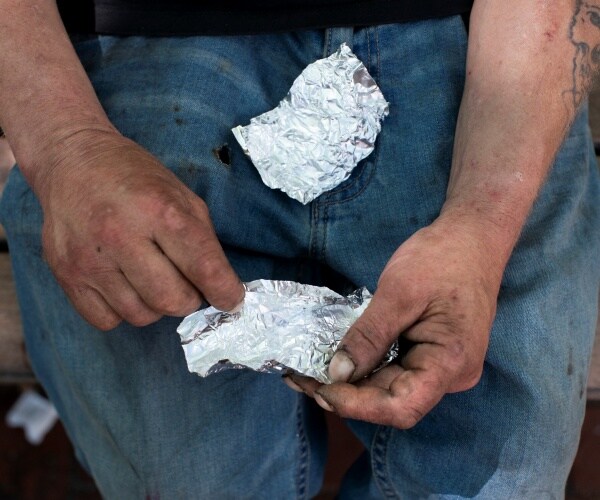 A man prepares to smoke fentanyl on a park bench