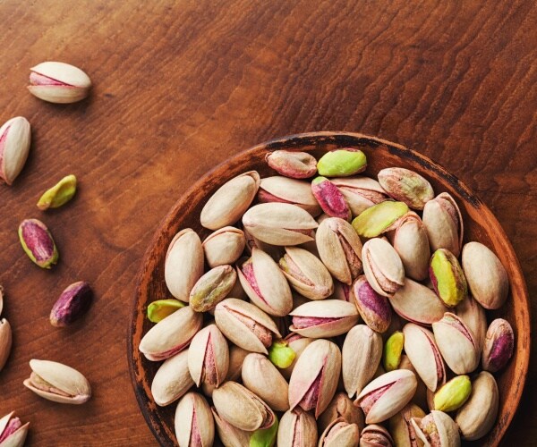 bowl of pistachio nuts in shells and out of shells and some on table next to it