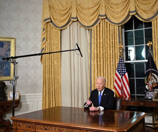 biden sitting in the oval office behind the resolute desk with a boom microphone mounted above him