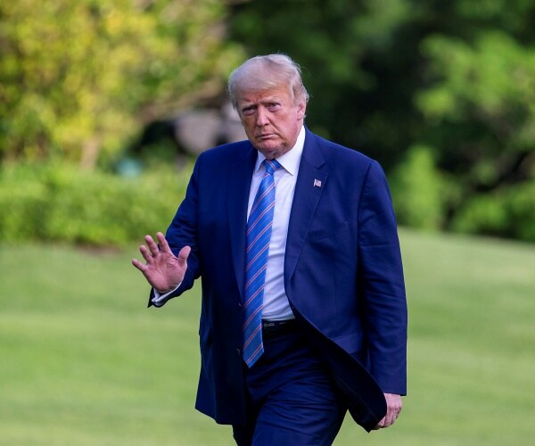 trump in a navy blue suit and blue striped tie walking on white house lawn