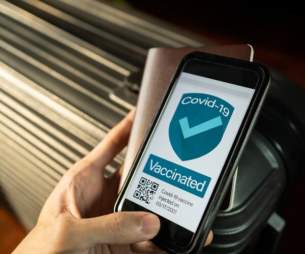 man holding phone showing vaccine passport in front of suitcase