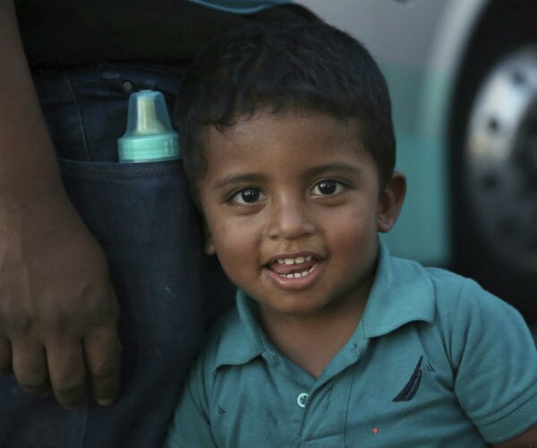  a migrant child looks at the camera as he waits with his family, outside at an immigration center 