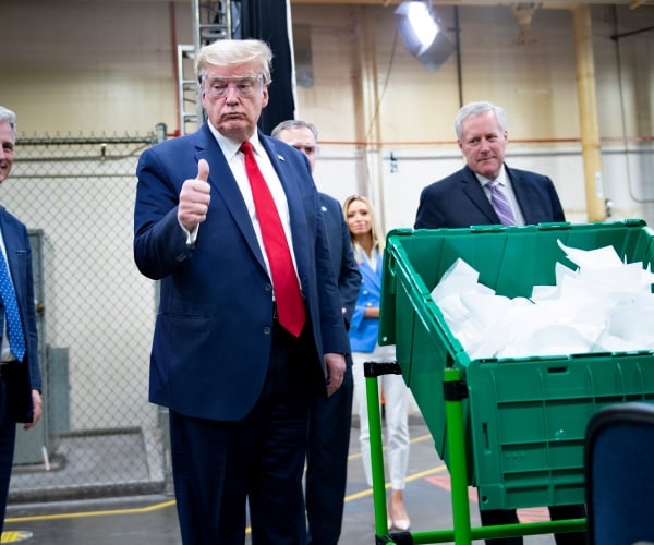 trump gives a thumbs up wearing a suit and red tie while visiting a mask factory in arizona