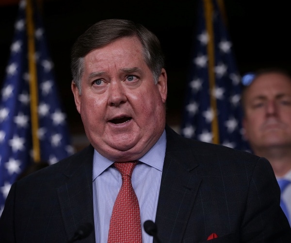 calvert in a suit, blue shirt, and red tie