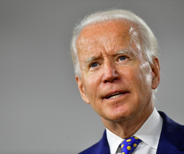 biden in a suit and blue patterned tie with gray background