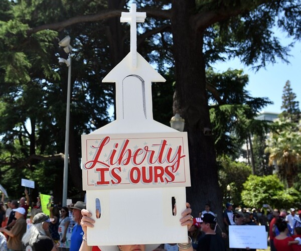 a woman holds up a church sign in protest to stay-at-home orders