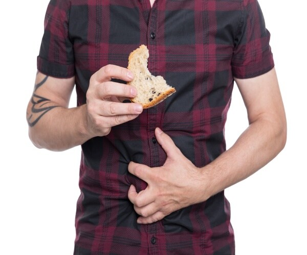 man clutching stomach while eating white bread