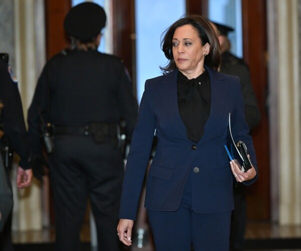 harris in a navy blue suit and black top walking through a hall