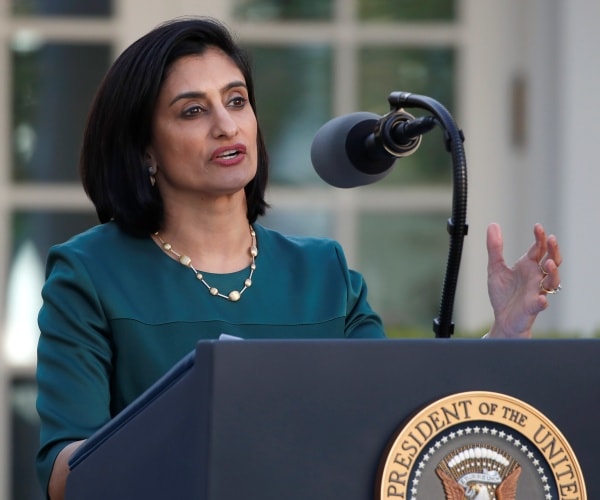 seema verma in a teal dress and necklace speaking outside