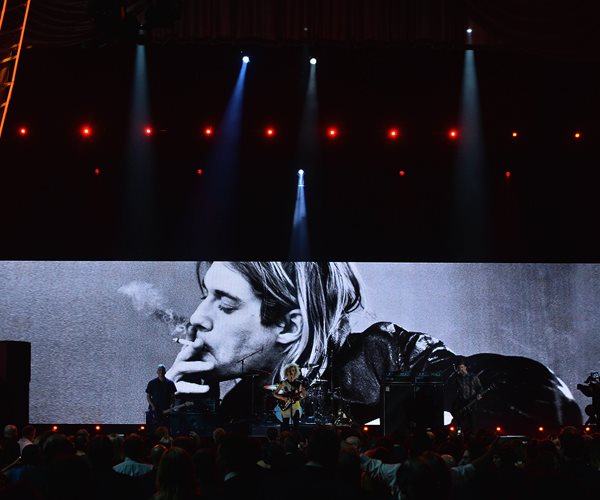 band on stage with photo of kurt cobain in background