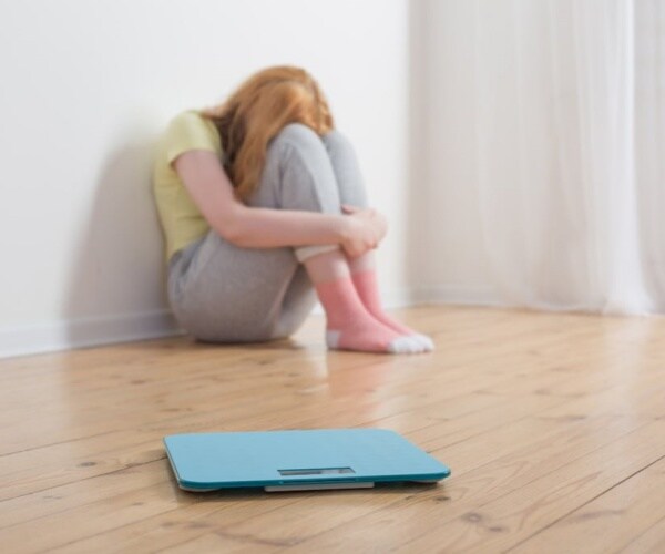 young woman on floor near scale with head in hands, upset