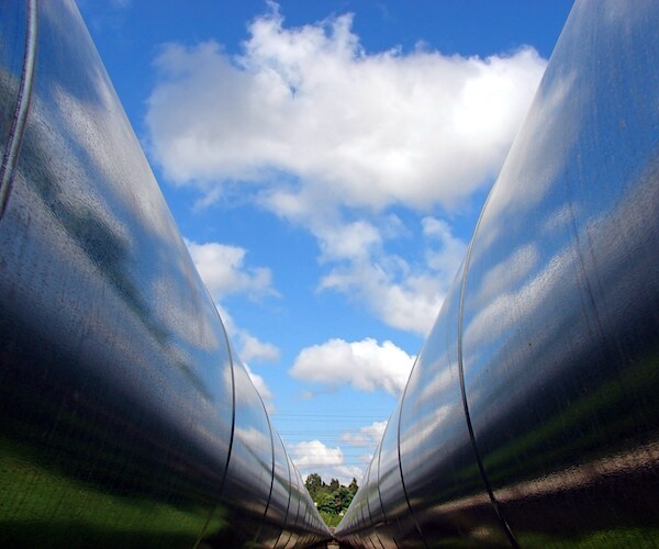 two large metalic pipelines reflect a bright blue sky