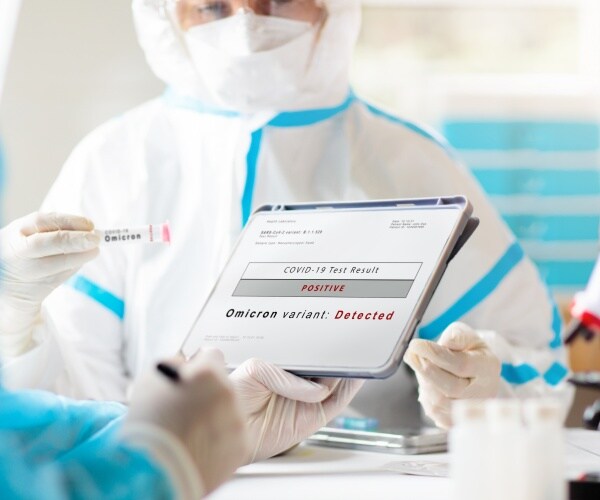 two scientists in a lab in protective gear looking at tablet screen that says 'omicron variant detected'