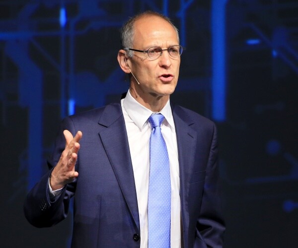 emanuel in a navy blue suit and light blue tie speaking on stage