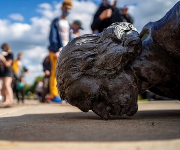 columbus statue fallen face to the ground with protesters standing around