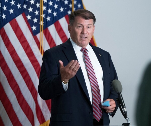 mike rounds stands in front of flags