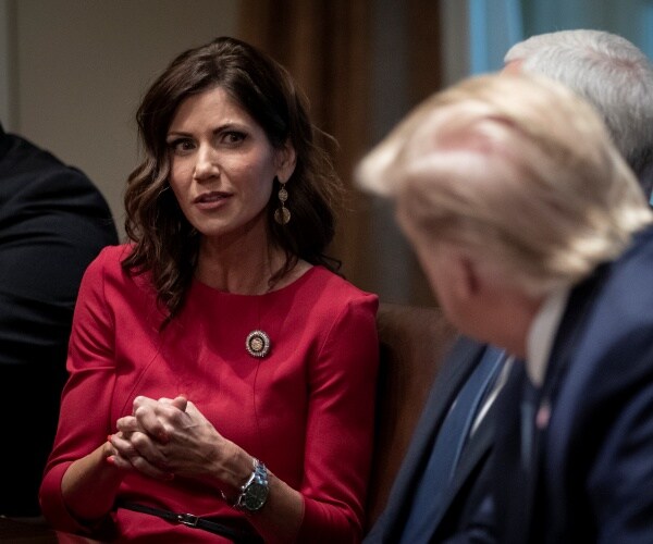 noem in a red dress sitting down talking to trump