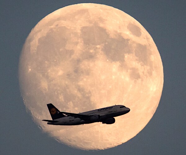 a plane flies in front of a large moon in the dusk sky