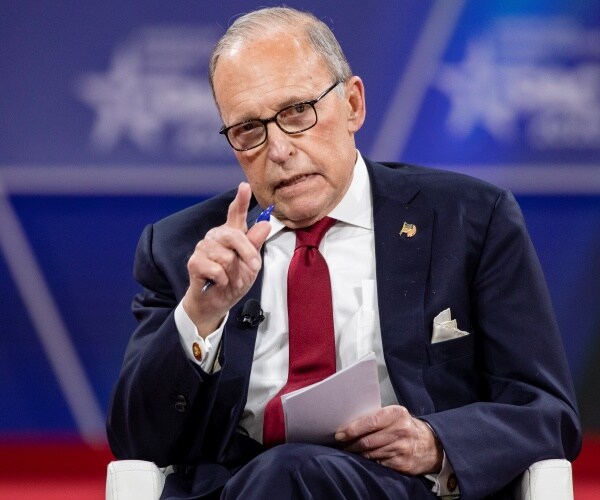 kudlow in a navy blue suit and red tie speaking at cpac sitting down