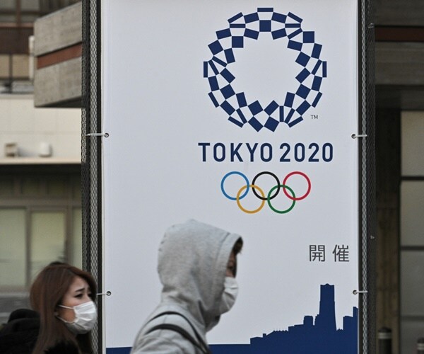 pedestrians in tokyo wear masks and walk past a 2020 olympic sign