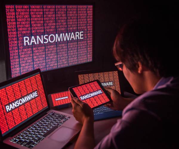 a person looking at multiple computers and devises with ransomware written on the screens