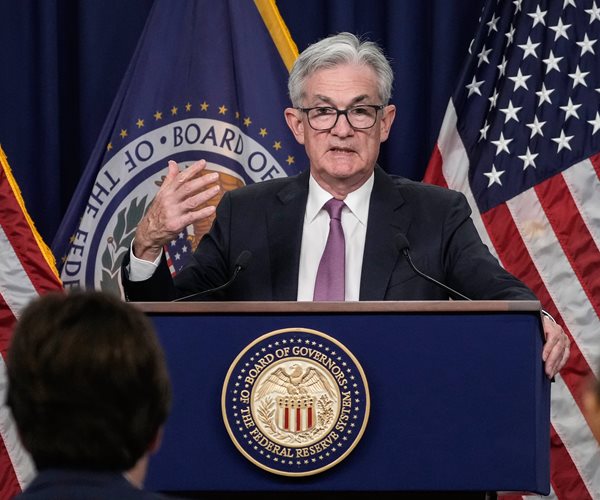 jerome powell speaks at a podium in front of flags